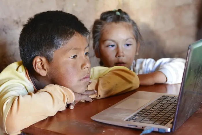 Two kids stare at a laptop.